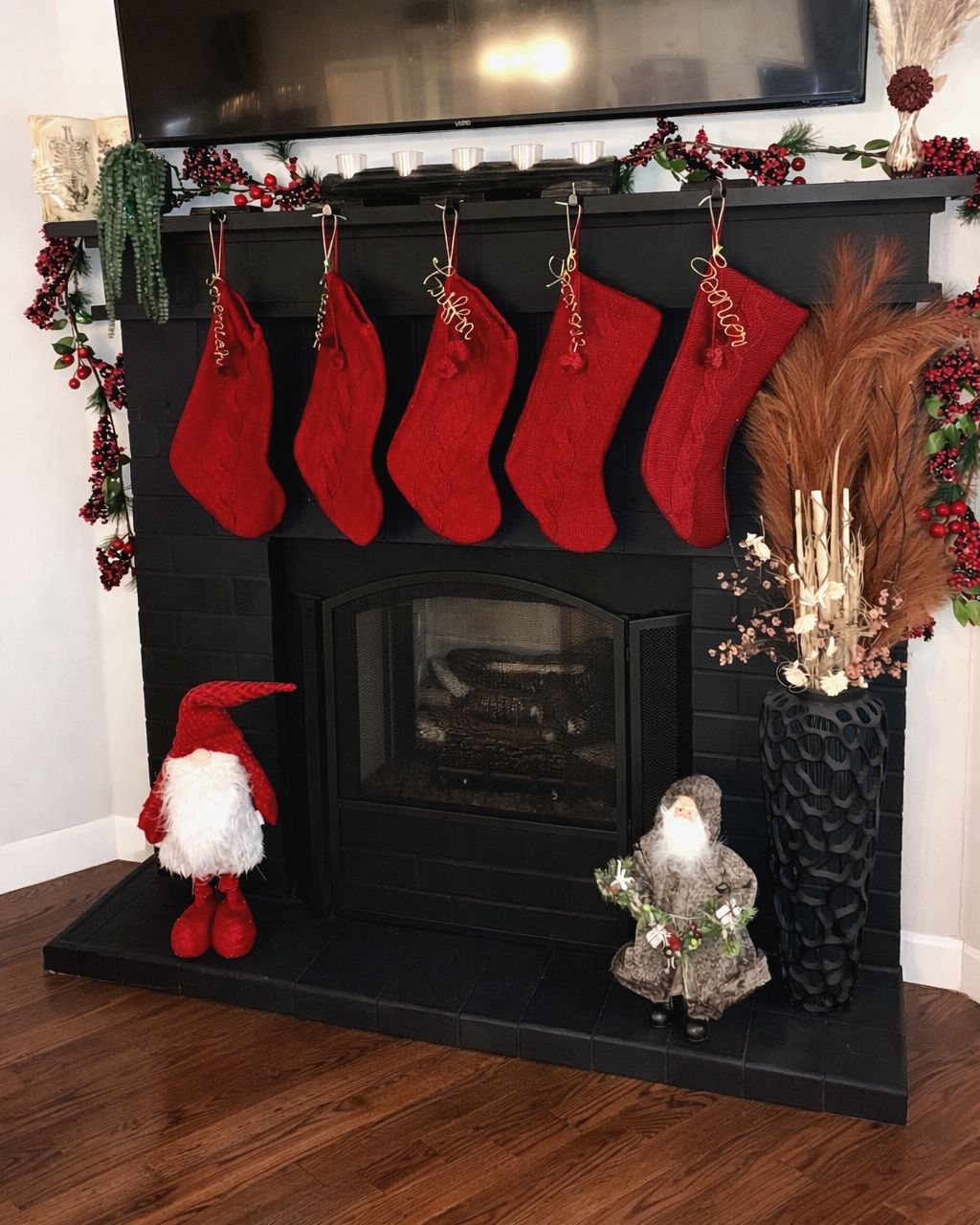 Black brick fireplace with five red knit stockings, berry garland, pampas grass and gnome figures