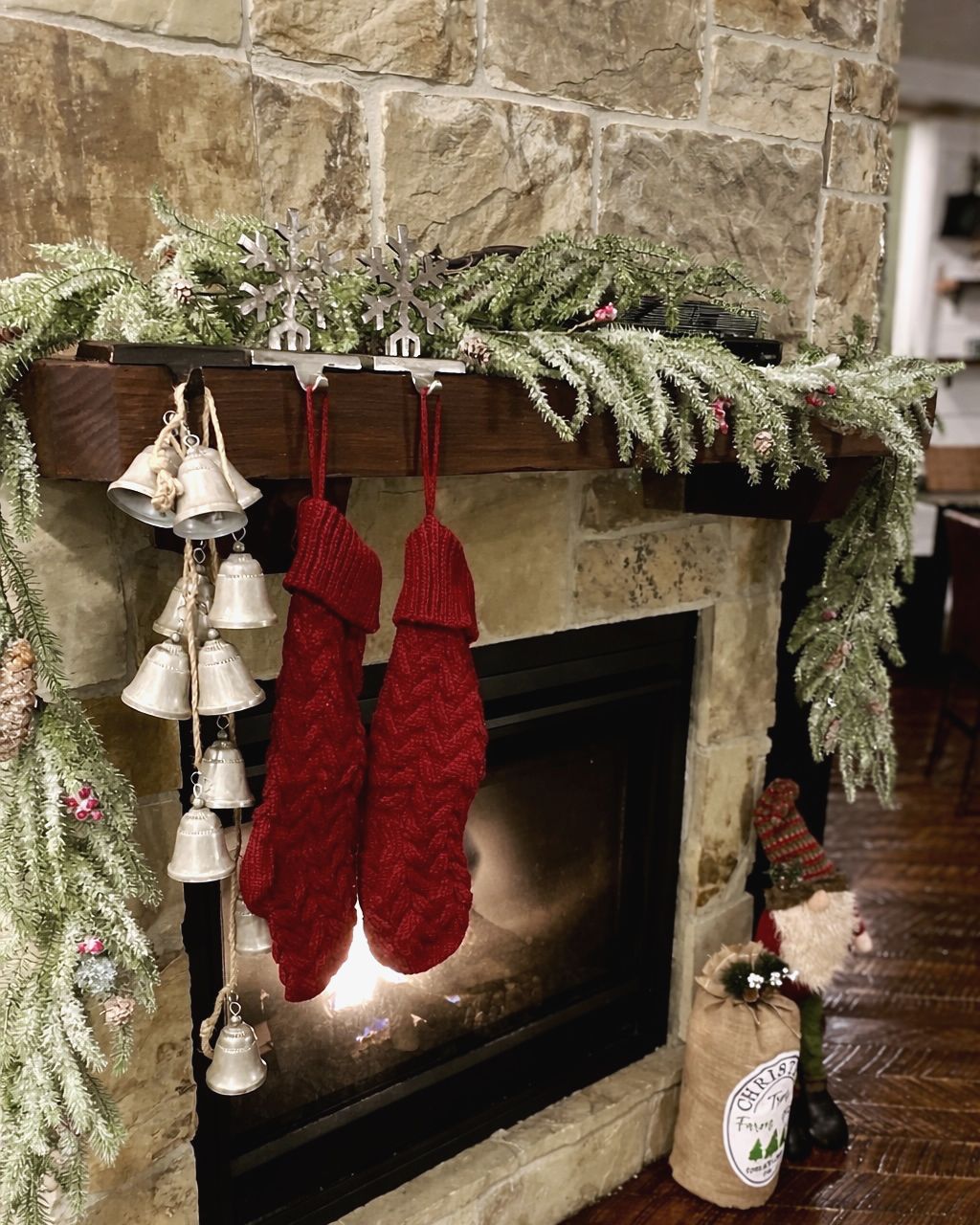 Stone fireplace mantel with frosted garland, red knit stockings, silver sleigh bells and a Christmas gnome